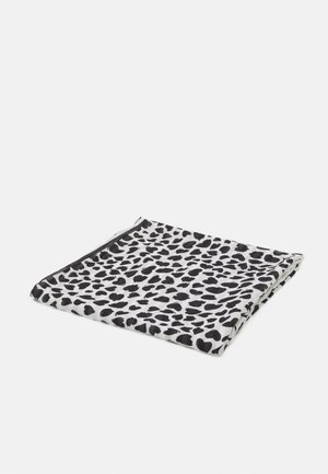 Tissu blanc plié avec des taches noires irrégulières ressemblant à un imprimé léopard, présenté sur un fond gris clair uni.