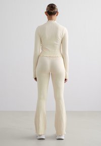 Top a maniche lunghe a coste color crema e pantaloni a palazzo con bordi ondulati, che mettono in risalto una finitura testurizzata e una silhouette aderente.
