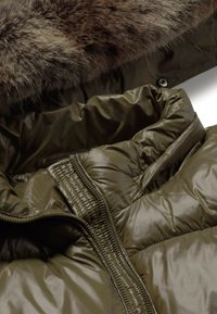 Doudoune vert olive avec un large col et une bordure en fausse fourrure marron sur la capuche, mettant en valeur les détails de la fermeture éclair et de la texture du tissu.