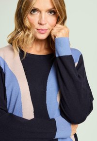 Suéter de punto con diseño de bloques de color en azul marino, azul claro y beige, con un ajuste relajado y puños acanalados. Textura suave.