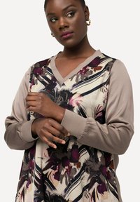 Bluzka z długim rękawem wykonana z lekkiego materiału, ozdobiona kwiatowym wzorem w odcieniach burgundu, beżu i czerni, z dekoltem w kształcie litery V oraz mankietami.