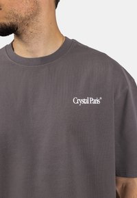 Šedé bavlněné tričko s volným střihem, na levé hrudi s bílým logem "Crystal Paris". Hladká textura a kulatý výstřih.