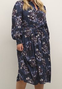 Bloemen blousejurk in marineblauw, met grote bloemenpatronen, een ceintuur in de taille, lange mouwen en gestructureerde manchetten. Zachte stof.