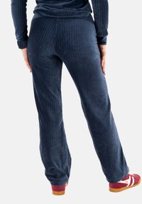 Pantalones de pana de color navy con textura de ribete vertical; ajuste holgado, ligeramente acampanados en el dobladillo, combinados con zapatillas deportivas rojas y blancas.