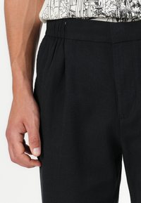 Pantalons noirs à coupe décontractée, dotés d'une taille élastique. Le tissu a une texture lisse et des poches de chaque côté.