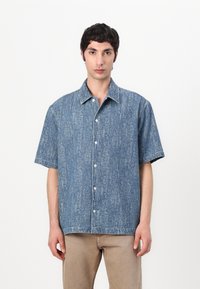 Camicia a maniche corte in denim azzurro chiaro con un motivo testurizzato, apertura frontale a bottoni e colletto classico. Dettaglio di cuciture bianche sottili.