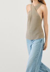 Knit halter top in light beige with a cross-over design at the neck; paired with light blue high-waisted jeans. Smooth texture.