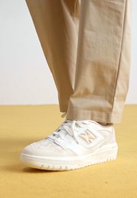 Λευκό αθλητικό παπούτσι με υφασμάτινη πλέξη και λείο δέρμα, που διαθέτει λογότυπο σε ανοιχτό καφέ απόχρωση και στερεή καουτσούκ σόλα.