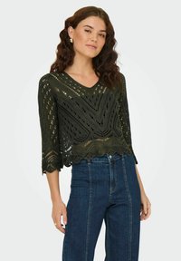 Pull en crochet vert foncé avec un décolleté en V, des manches trois-quarts et un ourlet en dents de scie. Présente des motifs ajourés dans tout le vêtement.