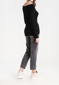Schwarzer, gerippter Off-Shoulder-Pullover kombiniert mit grauer Jeans und weißen Plateau-Sneakern. Das Outfit zeichnet sich durch lässige, entspannte Passformen aus.