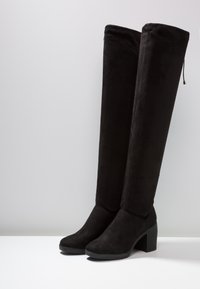 Paire de bottes noires en suède jusqu'au genou avec des talons blocs, des bouts ronds et un détail de lacet à l'arrière.