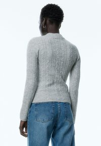 Grauer Strickpullover mit strukturiertem Rippmuster, lange Ärmel und runder Ausschnitt. Kombiniert mit blauen, hochtaillierten Jeans.