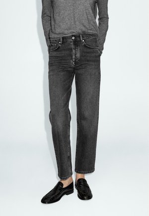 Donkergrijze denim jeans met een rechte snit, voorzien van vijf zakken en een knoopsluiting. Gecombineerd met zwarte mocassins.