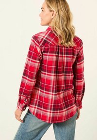 Red and black plaid flannel shirt with long sleeves, button cuffs, and an elongated back hem; soft texture with visible patterns.