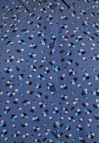 Blauer Stoff mit kleinem schwarzem, weißem und blauem Blumenmuster und blauen Knöpfen in der Mitte.