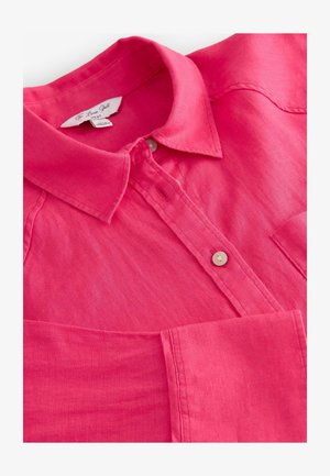 Vaaleanpunainen liinapaita, jossa on kauluksen muotoinen kaulus, nappisuljenta ja etutasku. Paita on sileää kangasta ja siinä on hienovarainen kiilto.