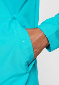 Lichtgewicht turquoise jas met een strak ontwerp, voorzien van een zijzak en een knoopsluitingdetail. Glad textuur van de stof.