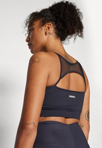  Sujetador deportivo negro con espalda de malla, que presenta tirantes finos y un logo en la parte inferior de la espalda. Textura suave, diseñado para ropa deportiva.