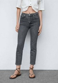 Jeans de tiro alto grises con un corte slim, que cuentan con bolsillos delanteros y cierre de botón. Combinados con sandalias marrones de tiras.