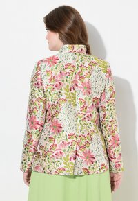 Giacca con stampa floreale realizzata in tessuto con fiori rosa e verdi su uno sfondo chiaro, dotata di un colletto alto e di uno spacco centrale sul retro.