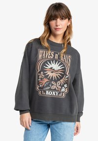 Felpa grigio scuro con maniche lunghe, colletto a girocollo e una stampa grafica floreale con il testo "Waves n' Rays" e "Roxy" in basso.