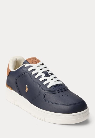 Ναυτικό μπλε δερμάτινο αθλητικό παπούτσι με λευκά κορδόνια, λευκή σόλα, καφέ λεπτομέρειες στη φτέρνα και στη γλώσσα, και ένα μικρό κεντημένο λογότυπο στο πλάι.