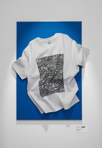 Hvit kortermet t-skjorte med svart doodle-stil trykk. Vist mot en livlig blå bakgrunn som fremhever designet.
