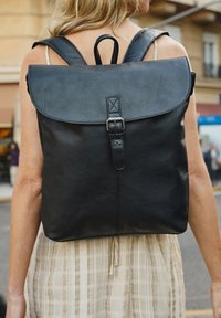 Melnas ādas mugursoma ar noapaļotu vāku, regulējamām jostām un sprādzi. Gluda tekstūra ar minimālistisku dizainu un šuvēm.