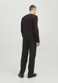 Maglione lavorato a maglia di un viola scuro, con maniche lunghe, collo a giro e polsini a coste, abbinato a pantaloni e scarpe neri.