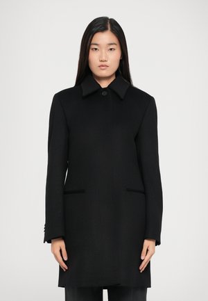 Manteau en laine noir avec un col classique, fermeture à un seul bouton et deux poches avant. Il présente des manches longues et une coupe ajustée.
