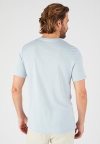 T-shirt azzurro chiaro a maniche corte con scollatura rotonda, caratterizzato da una texture morbida e un orlo dritto, indossato con pantaloni beige.