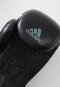 Zwarte bokshandschoenen met gaasstof, voorzien van een gevoerde ronde knokkels beschermd en het Adidas-logo in teal. Compac te, ergonomisch ontwerp.