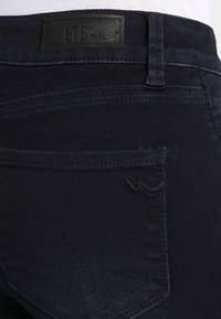 Mörkblå denimjeans med en slät textur, med en läderetikett vid midjan och subtila sömnadsdetaljer nära bakfickan.