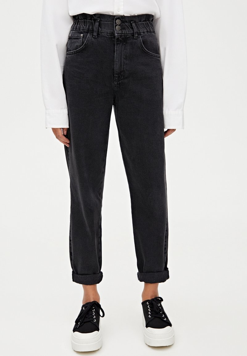 Jean en denim noir taille haute avec une coupe décontractée, ourlets retroussés et poches avant, associé à des baskets noires à semelles blanches.