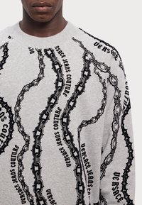 Sudadera gris con un patrón de cadenas y texto en negro. Cuello redondo y mangas largas, con un ajuste relajado y tejido texturizado.