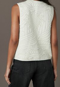 Gepolsterte Weste in Off-White mit strukturierten Wellenmustern und einem Sonnendesign auf der Rückseite. Legere Passform mit abgerundetem unteren Saum.