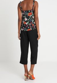 Mustat kukkakuosiset hihattomat paidat ohuilla olkaimilla, paljastava selkä. Yhdistetty mustiin cropped-housuihin ja oransseihin korkeatukki-korkokenkiin.