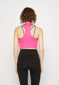 Top corto rosa con design a racerback, caratterizzato da sottili spalline grigie sotto. Un paio di leggings neri a vita alta.