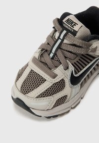 Nike-Laufschuh in Grau und Beige, mit Mesh-Einsätzen, strukturierten Schnürsenkeln und einem schwarzen Swoosh-Logo. Mit gepolstertem Sohlen.