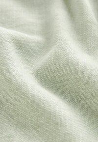 Tissu texturé vert clair avec un motif tissé fin, affichant une douceur et un léger éclat. Le matériau semble léger et respirant.