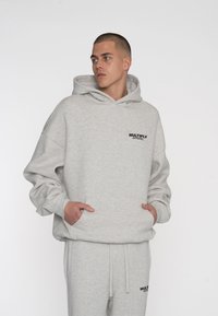 Grauer Kapuzenpullover mit lockerer Passform, aus weichem Stoff gefertigt, mit einer Vordertasche und schwarzem "MULTIPLY APPAREL" Logo auf der Brust.