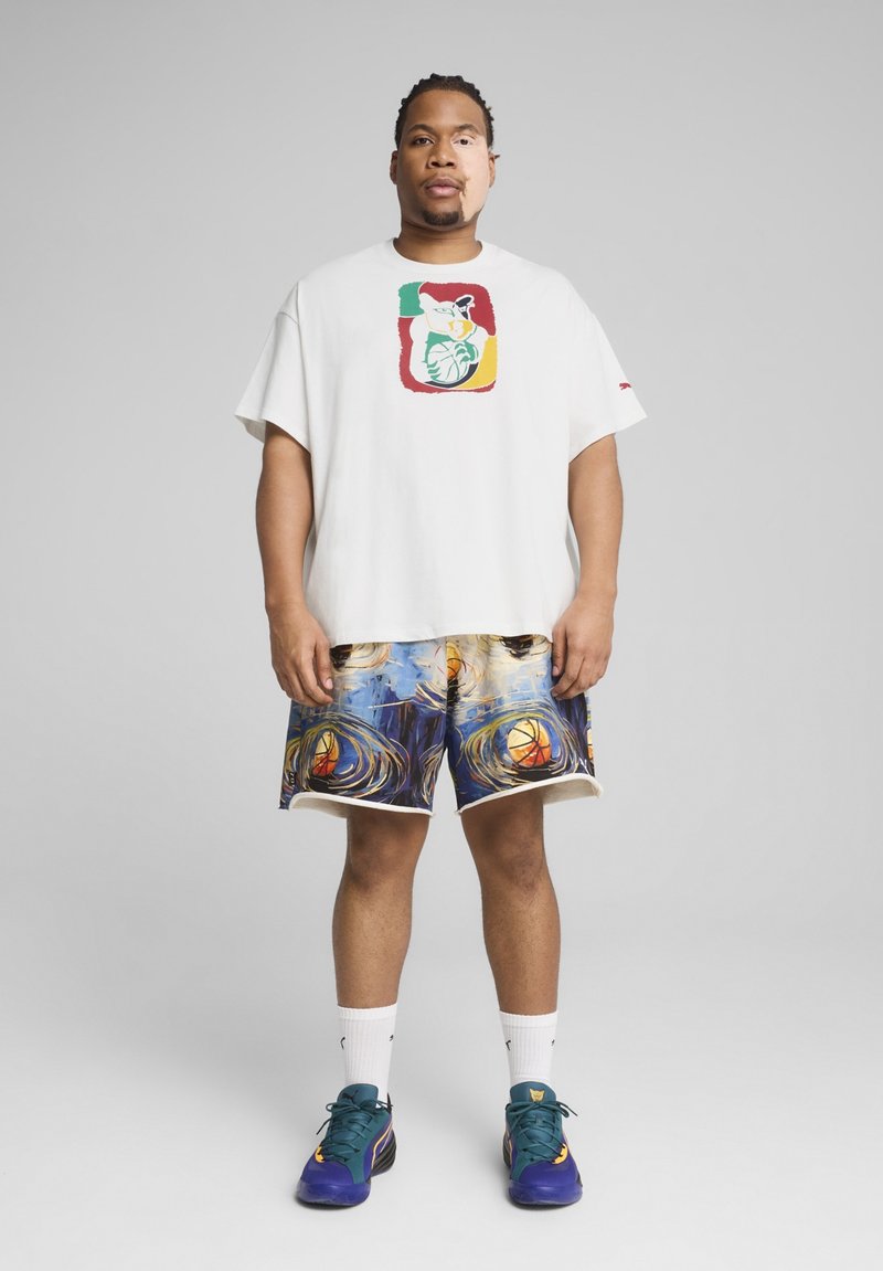 Tricou alb supradimensionat cu imprimeu grafic colorat, asociat cu pantaloni scurți multicolori, cu un model ce include motive de baschet și detalii decorative.