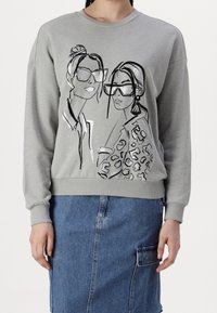 Sudadera gris con escote redondo, que presenta dibujos lineales en negro de dos mujeres, una con estampado de leopardo. Textura suave, puños y bajo de canalé.