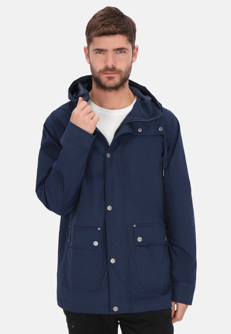 Marineblaue wasserdichte Jacke mit Kapuze, Druckknöpfen und zwei Fronttaschen. Glatte Textur und lässige Passform. Darunter ein weißes T-Shirt mit Rundhalsausschnitt.