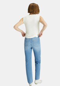 Jeans dritti azzurri chiari in denim, con vita media e due tasche posteriori. Indossati con un top bianco senza maniche.