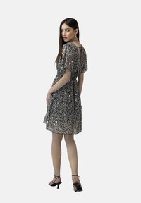 Vestido negro de flores con mangas cortas, de tejido ligero y con detalle de abertura en la espalda. Combinado con tacones negros de tiras.