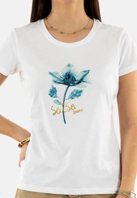 Camiseta de algodón blanca con un estampado floral azul y el texto dorado "Sense Jeans". El diseño incluye pétalos y hojas delicadas.