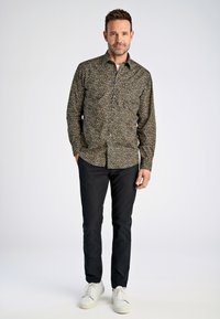 Camisa de botones con un patrón floral oscuro, con flores amarillas y blancas, combinada con pantalones negros y zapatillas blancas, en una postura de pie.