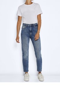 T-shirt rosa chiaro a maniche corte abbinato a jeans blu slim-fit. I jeans presentano una finitura sbiadita e un design classico a cinque tasche. Sneakers bianche.