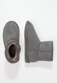 Stivali alla caviglia in suede grigio con morbida fodera in pelliccia, punta arrotondata e suola in gomma texturizzata. Presentano dettagli cuciti lungo le cuciture.